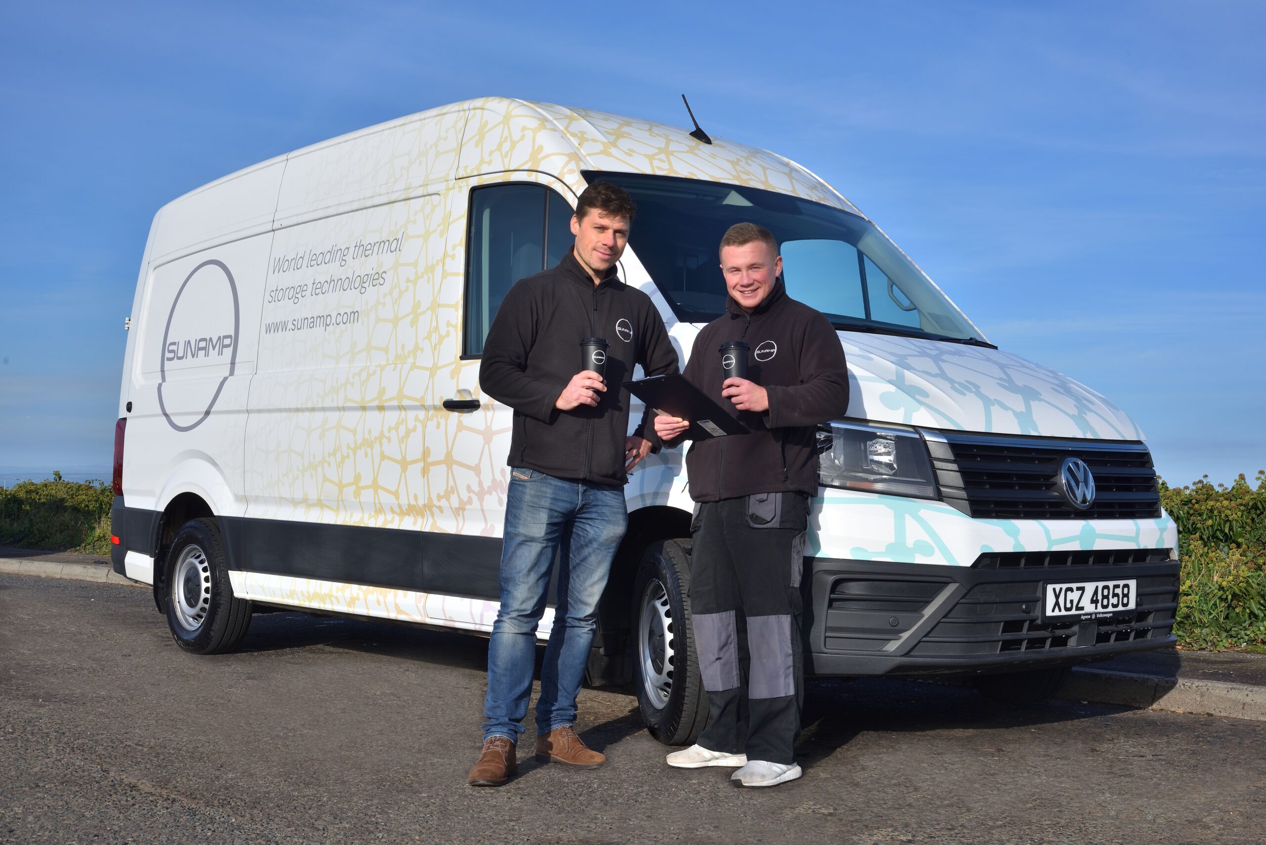 Two installers standing in front of Sunamp branded van, holding coffee cups and clipboards, wearing Sunamp branded clothing