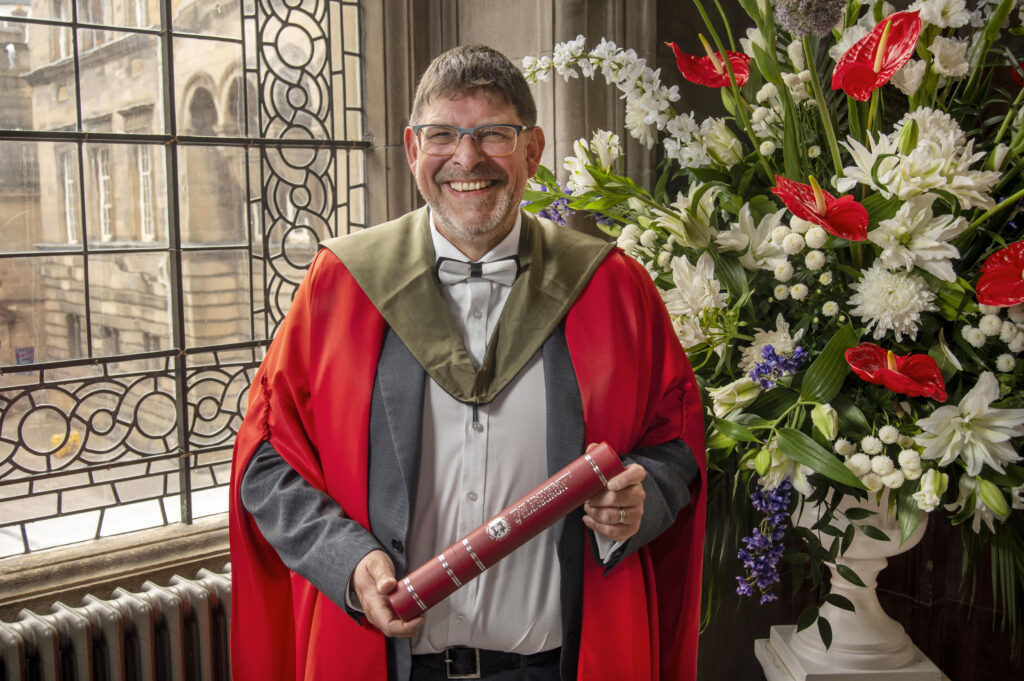 Andrew Bissell in graduation robe holding scroll